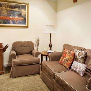 A cozy living room with a comfortable sofa and armchair, decorated with colorful cushions and a stylish lamp beside a framed artwork.