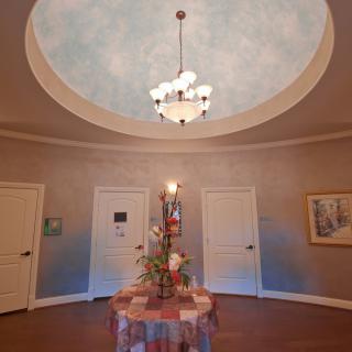A decorated circular room with a chandelier hanging from the ceiling, featuring a central table adorned with flowers and surrounded by multiple doors.