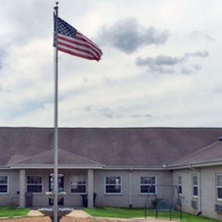An American flag proudly waves in front of a building under a cloudy sky.