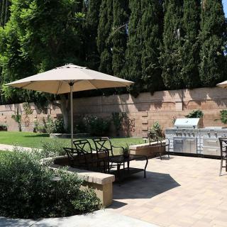 A well-maintained backyard with a patio featuring outdoor seating, a large umbrella, and a grill area.