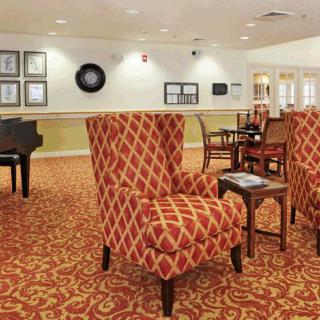 A cozy lounge area with patterned chairs, tables, and a grand piano.