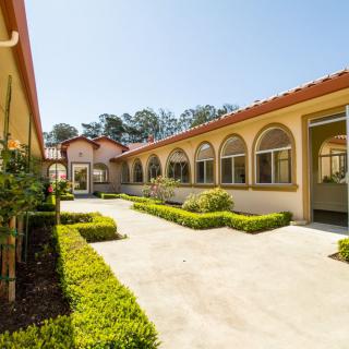 A sunny courtyard surrounded by a building with arched windows and well-maintained landscaping.