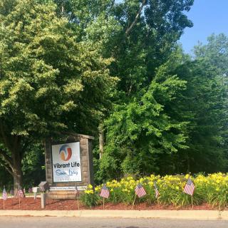 A park entrance sign surrounded by trees and vibrant yellow flowers.