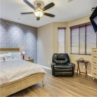 A cozy bedroom with a wooden bed, an armchair, and a ceiling fan.