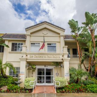 A building entrance with well-maintained landscaping and a flag displayed, set against a cloudy sky.