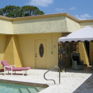 A sunny patio with a pool, lounge chair, and an umbrella-covered seating area.