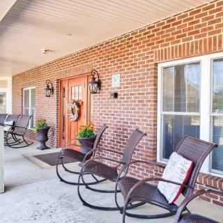 A cozy porch area featuring several rocking chairs, a brick facade, and decorative elements by the front door.