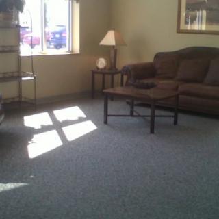 A cozy waiting room with a sofa, lamp, and table next to a window letting in sunlight.