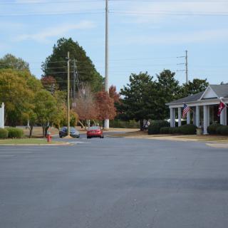 A suburban street with cars parked on the side, framed by residential buildings and trees.