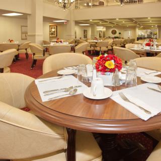 An elegantly set dining area with neatly arranged tables and chairs, adorned with floral centerpieces.