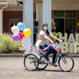 A woman joyfully rides a decorated bicycle with colorful balloons to celebrate a birthday.