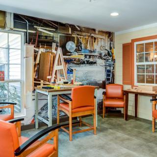 A cozy workshop interior featuring orange chairs, a workbench, and tools organized on the wall.