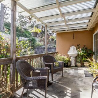A cozy patio with wicker chairs and a fountain, surrounded by lush plants under a clear roof.