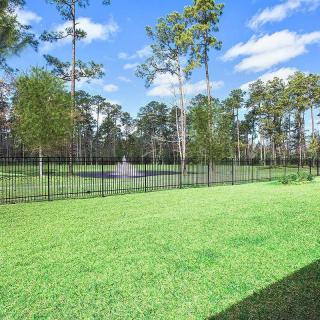 A scenic backyard with a view of a pond and surrounding trees, enclosed by a fence.