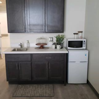 A small kitchenette with dark cabinets, a microwave on top of a mini refrigerator, and decorative plants.