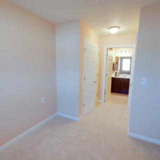 A view of a carpeted hallway leading to a bedroom with an attached bathroom.