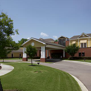 A view of a building entrance with a landscaped driveway and clear sky.