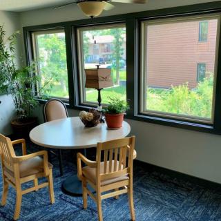 A cozy meeting area with a round table, chairs, and large windows providing natural light.