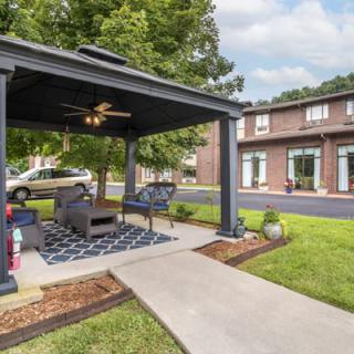 A modern gazebo with comfortable seating is set in a green lawn, adjacent to a contemporary building.