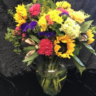 A vibrant bouquet of various flowers, including sunflowers and colorful blooms, displayed in a glass vase.
