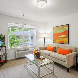 A modern living room with a beige sofa, colorful pillows, and a vibrant painting on the wall.