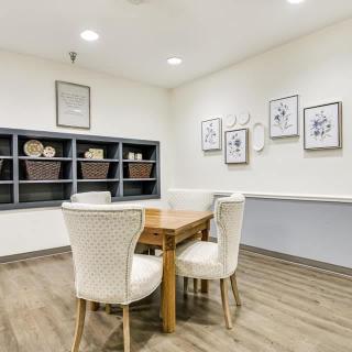 A cozy, modern room with a wooden table and upholstered chairs, adorned with decorative shelving and framed artwork.