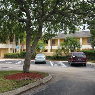 A small parking lot with parked cars in front of a two-story building surrounded by trees.