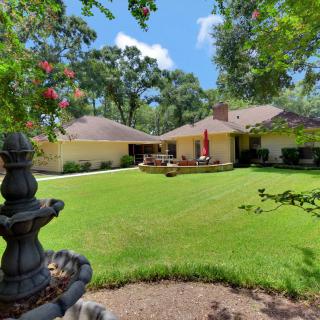 A sunny backyard with a well-maintained lawn, patio area, and surrounding trees.