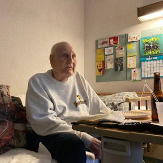 An elderly man sits quietly in a hospital room, engaged in reading beside a bedside table.