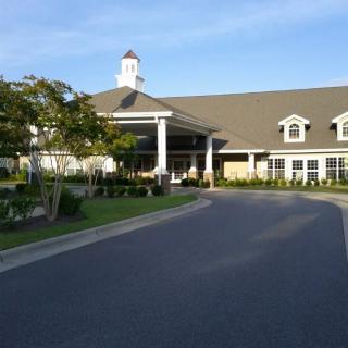 A large building with a driveway and landscaped gardens under a clear blue sky.