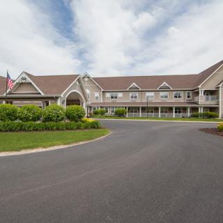 A large building with a curved driveway, landscaped greenery, and an American flag under a cloudy sky.