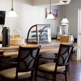 A cozy cafe interior with chairs around a wooden counter, featuring pastries and warm lighting.