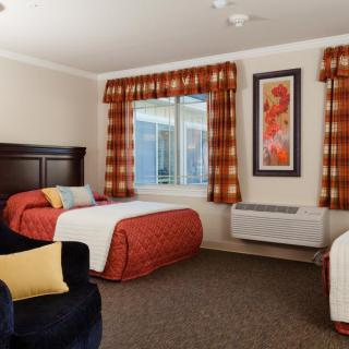 A cozy hotel room with twin beds, decorated with warm colors and featuring a large window.