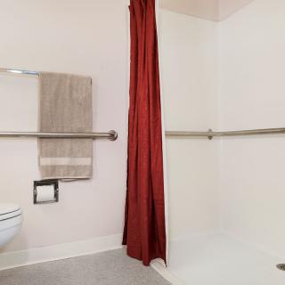 An accessible bathroom with a red shower curtain and grab bars.