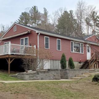 A red house with a porch and deck, surrounded by trees in a rural setting.