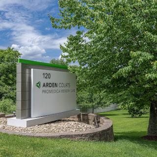 A sign for a business surrounded by lush greenery and a partly cloudy sky.