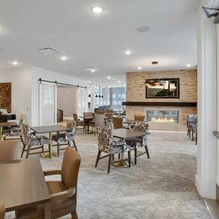 A modern seating area with tables and chairs, featuring a fireplace and ample lighting.
