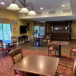 A cozy lounge and dining area with several tables and chairs, featuring a carpeted floor, a chandelier, and a television mounted on the wall.