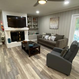 A modern living room with a cozy setup featuring a sofa, armchair, television above a fireplace, and wood flooring.