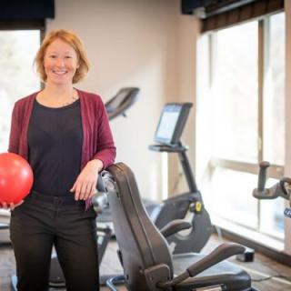 A person standing in a gym holding a red exercise ball.