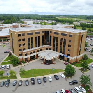 Aerial view of a modern hospital building surrounded by a parking lot and landscaped areas.