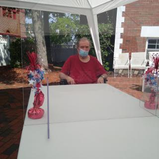 An elderly individual wearing a mask sits at a table adorned with festive decorations in an outdoor setting.
