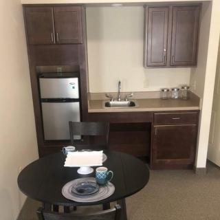 A small kitchenette with dark wood cabinets, a mini fridge, and a round table set for two.