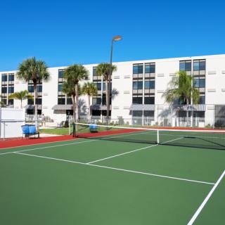 An outdoor tennis court located in front of a residential apartment building under a clear blue sky.