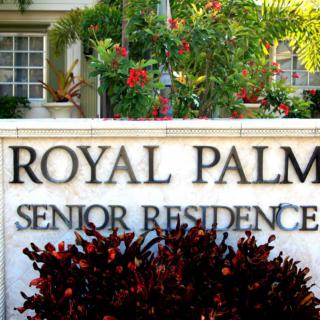 Entrance sign for Royal Palm Senior Residence surrounded by greenery.