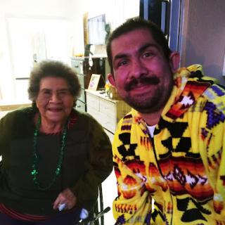 A joyful moment shared between an elderly woman and a young man, both smiling warmly in a cozy indoor setting.
