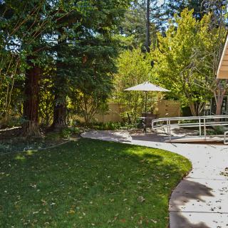 A serene garden setting with a pathway leading to an outdoor patio area under trees.