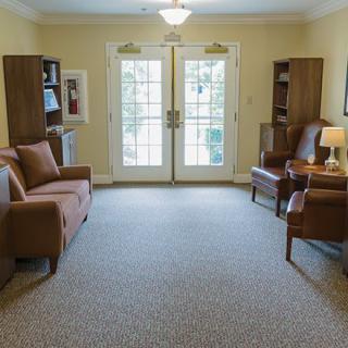 A cozy living room with sofas, chairs, and bookshelves facing glass doors.