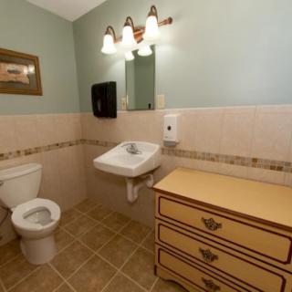 A clean and neatly organized bathroom with a sink, toilet, mirror, and a piece of furniture.