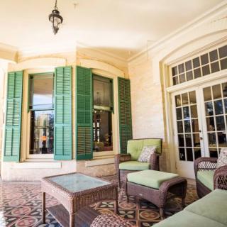 A cozy outdoor patio with wicker furniture and green shutters.
